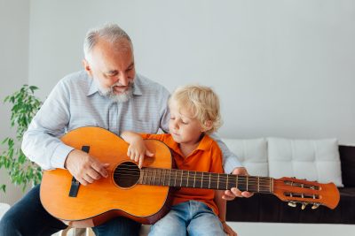 Happy grandpa teaching his grandson to play guitar